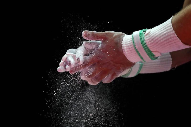 Un gymnaste se dépoussière les mains avec de la craie.