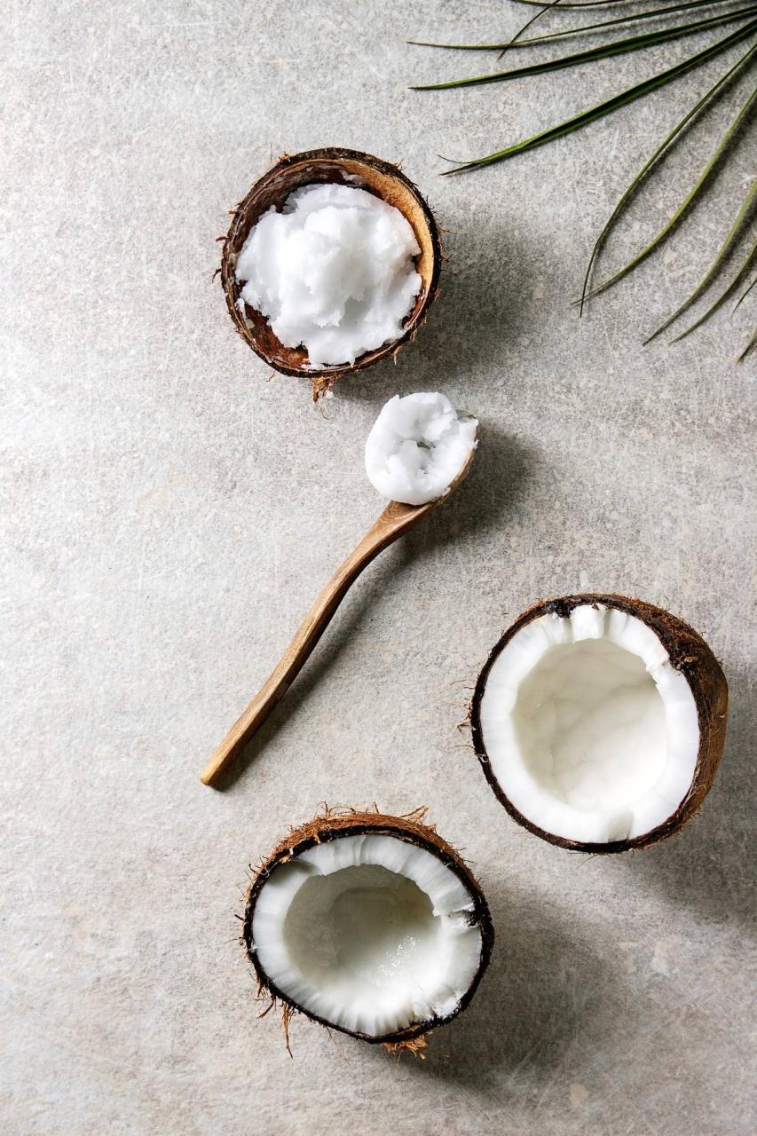 L'huile de noix de coco repose sur une cuillère à côté des noix de coco ouvertes.